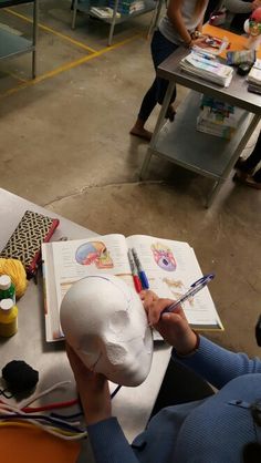 a person sitting at a table with a hat on it's head and an open book in front of them