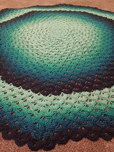 a crocheted blanket is sitting on the floor next to a brown and green rug