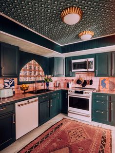 a kitchen with green cabinets, white appliances and a red area rug on the floor