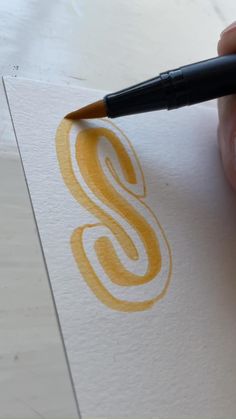 a person holding a pen and writing on paper with the letter s in yellow ink