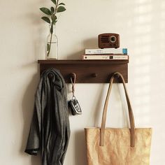 a brown bag hanging on a wall next to a wooden shelf with a camera and book