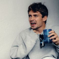 a man holding a blue cup in his right hand and making a funny face while sitting down