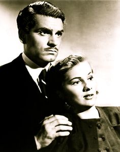 an old black and white photo of two people posing for the camera with one woman's arm around the man's shoulder