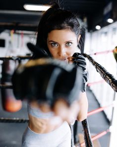 a woman wearing boxing gloves and holding a punching glove in her right hand while looking at the camera