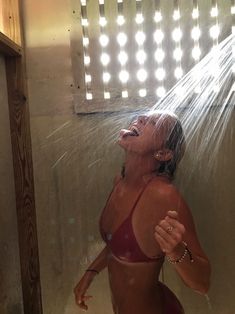 a woman in a red bathing suit standing under a shower head and spraying water on her face