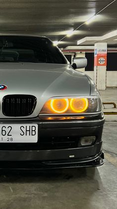 the front end of a silver bmw car in a parking garage with its lights on