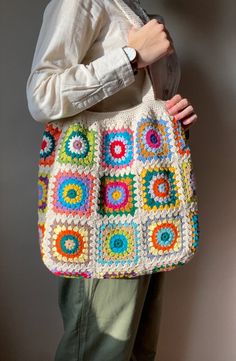 a woman holding a multicolored crocheted bag