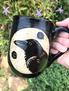 a hand holding a black coffee mug with a bird on it's face and moon in the background