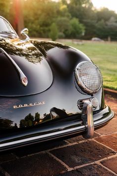 the front end of a black sports car parked on a brick road with grass and trees in the background