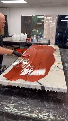 a man is working on a piece of art with red and white paint in the background