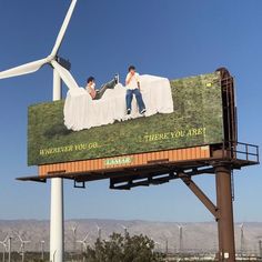 a billboard with two men laying on top of each other in front of windmills