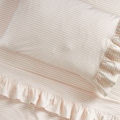 the bedding is made up with pink and white striped sheets, ruffled edges, and pillows