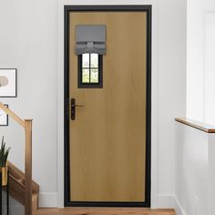 a wooden door in a white room next to a stair case and potted plant