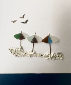 three beach umbrellas sitting on top of a white wall with birds flying above them