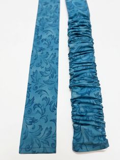 two blue ties with ruffled edges on a white table top, next to each other