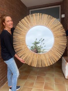 a woman holding up a large mirror made out of bamboo sticks in front of a brick wall