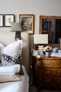 a white bed topped with lots of pillows next to a wooden dresser covered in pictures