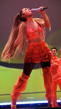 a woman with long hair wearing an orange outfit and holding a microphone in her hand