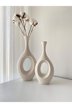 two white vases sitting next to each other on a table with flowers in them