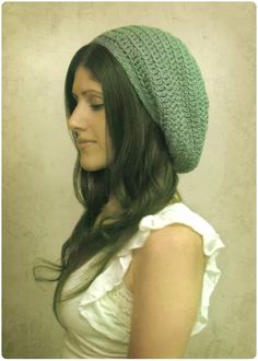 a woman with long hair wearing a green knitted hat and white shirt is looking away from the camera