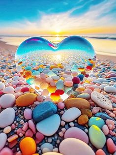 a heart shaped glass ball sitting on top of a beach covered in rocks and pebbles