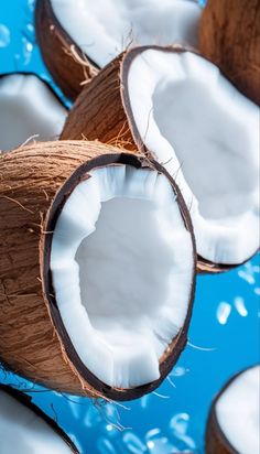 coconuts are shown on a blue surface with water splashing around them and one is cut in half