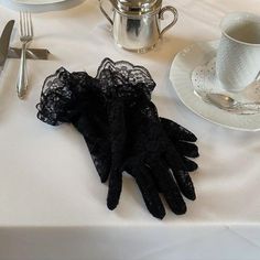 a table topped with white plates and silverware covered in black lace gloves next to a teapot