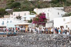 a group of people standing on top of a rocky beach next to a white building