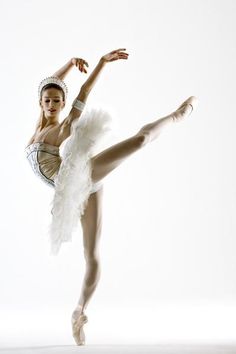 a ballerina in white tutu and feathered skirt posing with her arms stretched out