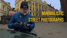 a man with a hat and glasses holding a camera in front of a building that says minimalistic street photographs