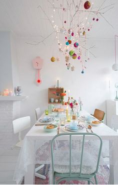 a dining room table is set with plates and bowls on it, surrounded by colorful ornaments hanging from the ceiling