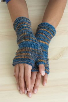 a woman's hands with blue and yellow knitted gloves on top of a wooden table