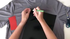 two hands are writing on a t - shirt with red and green paper next to scissors