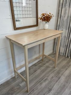 a wooden table sitting in front of a window next to a vase with flowers on it