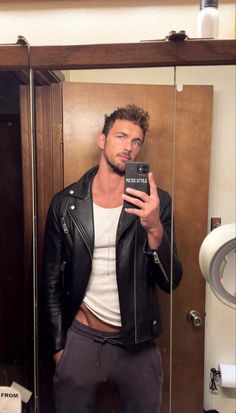 a man taking a selfie in front of a mirror wearing a leather jacket and sweatpants