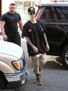 the two men are walking down the street with their cars behind them and one is wearing a black t - shirt