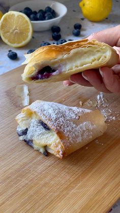 a person is holding a pastry with blueberries and powdered sugar on it as they sit on a cutting board