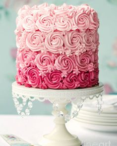 a pink and white cake with roses on it sitting on top of a table next to a plate