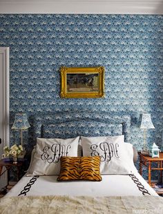 a bedroom with blue wallpaper and white bedding has a gold framed painting on the wall