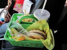 a green plastic basket filled with food next to a person holding a drink and cell phone