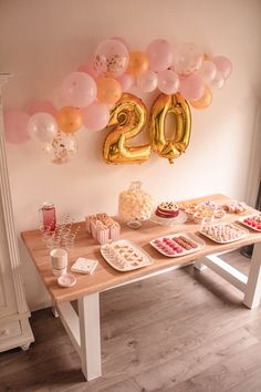 a table topped with lots of desserts and balloons next to a number twenty sign