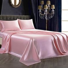 a bed covered in pink sheets and pillows next to a window with chandelier
