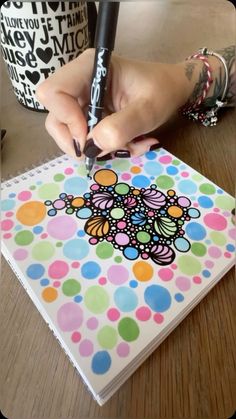 a person with a pen is drawing on a notebook that has polka dots and an image of a flower