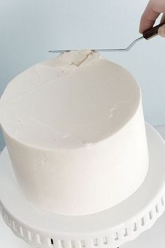 a person cutting into a white cake with a pair of scissors on the top of it