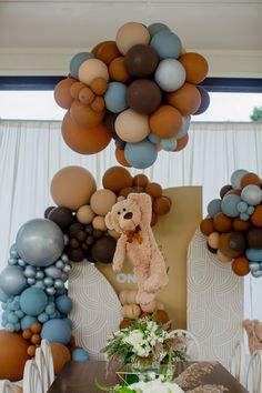a teddy bear hanging from the ceiling above a table with flowers and balloons on it