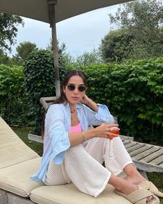 a woman sitting on top of a lounge chair holding a drink