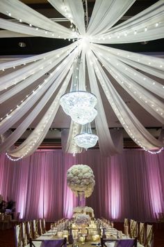 an elegant wedding setup with white drapes and chandelier hanging from the ceiling