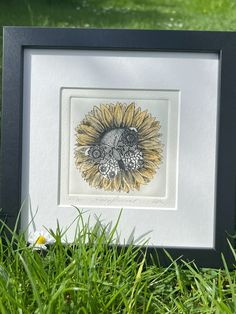 a sunflower is in the grass with a black frame and white border around it