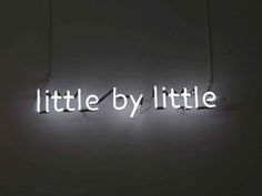 a neon sign that says little by little on the side of a wall in a dark room