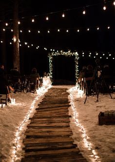 a snowy path is lit up with lights and garlands for an outdoor wedding ceremony